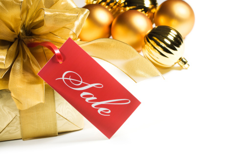 A sale tag label or sign on a Christmas gift wrapped in gold paper and ribbon, arranged with gold ball ornaments. Isolated on a white background.