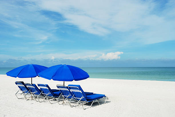 Blue beach umbrellas on a white sandy beach. Blue beach umbrellas and beach chairs on a pristine beach at seaside.  marco island stock pictures, royalty-free photos & images