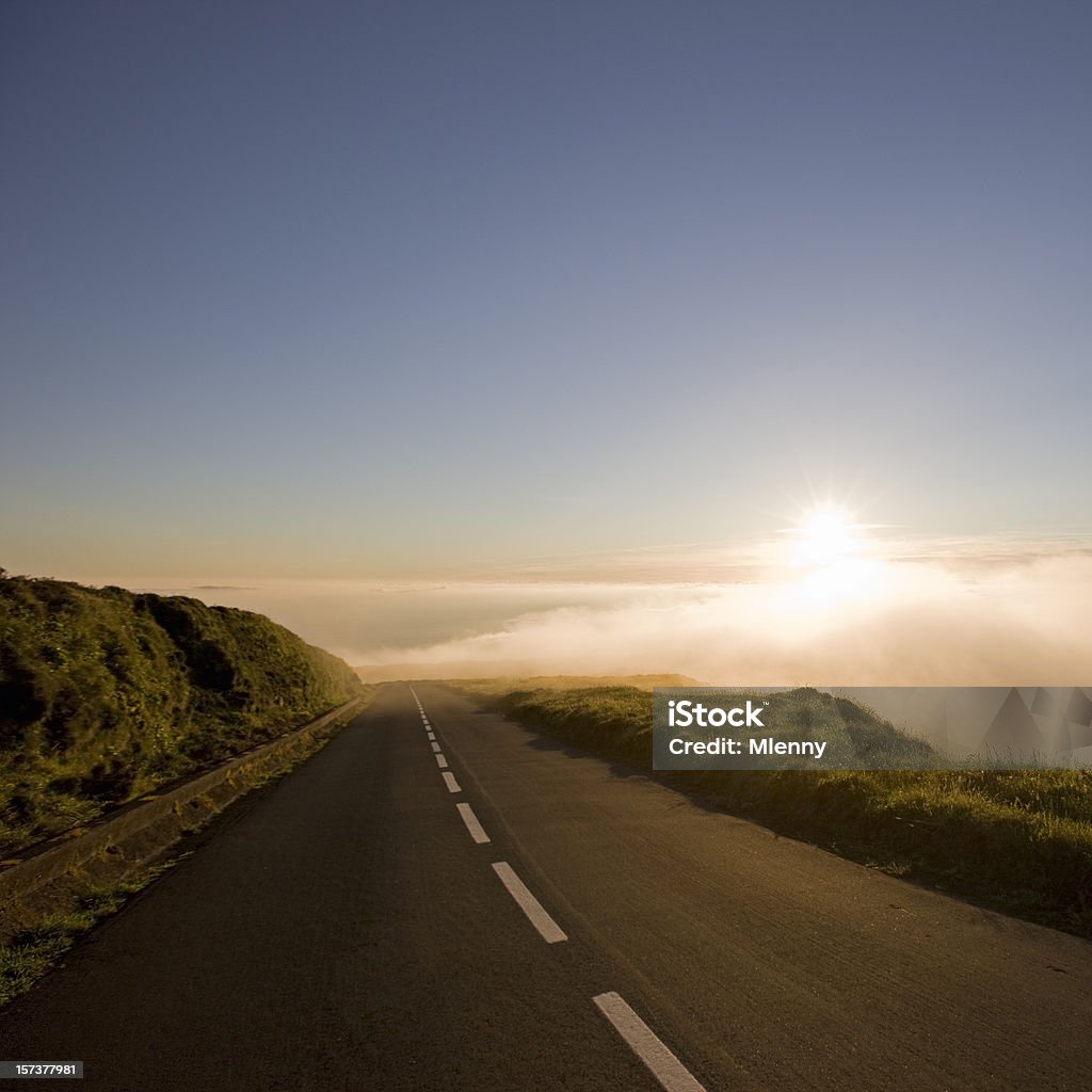 Country Highway into Clouds during Sunset Country Road leading towards the clouds -  fog  at the horizon during an amazing sunset. Sun shining over the cloudscape. Squared. Eternity Stock Photo