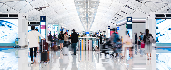 Motion blur of Asian tourist traveler people walk at Hong Kong airport terminal boarding gate, flight arrival departure information board. Air transportation, airline transport business, Asia travel