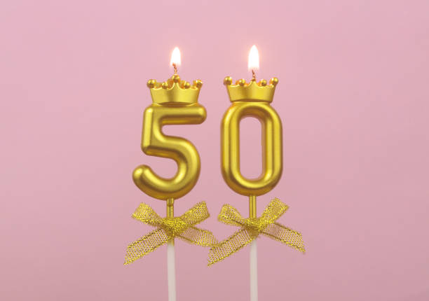 Gold birthday candles burning on pink, number 50. stock photo