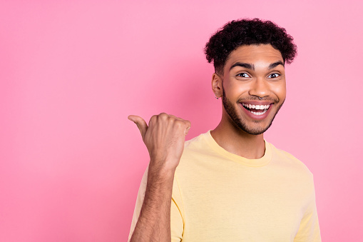 Photo of overjoyed impressed guy afro hairstyle dressed yellow t-shirt indicating at offer empty space isolated on pink color background.