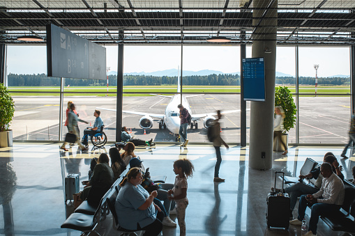 Diverse people sitting and standing at departures terminal. Each killing time their own way while waiting for their flight.