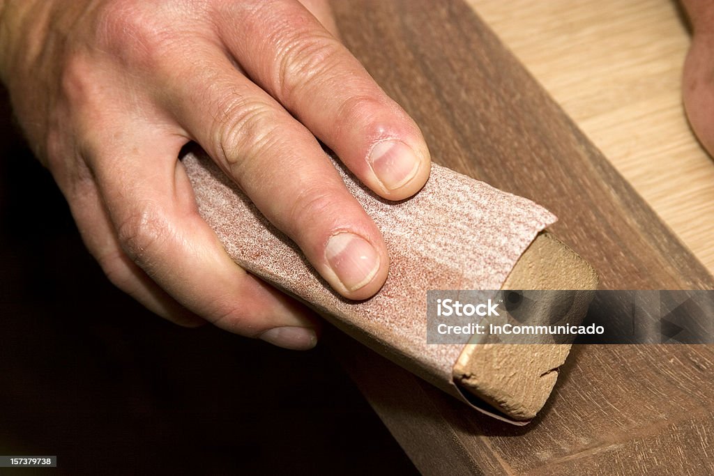 Close-up of a man sanding by hand in the workshop Furniture maker sands an unfinished piece of furniture to prepare it for finishing. Block Shape Stock Photo