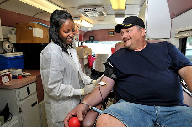 Blood donor man with nurse Doctor Phlebotomist working with blood donor in a portable bloodmobile. Need photos representing healthcare, particularly eye and dental? Please see these... bloodmobile stock pictures, royalty-free photos & images