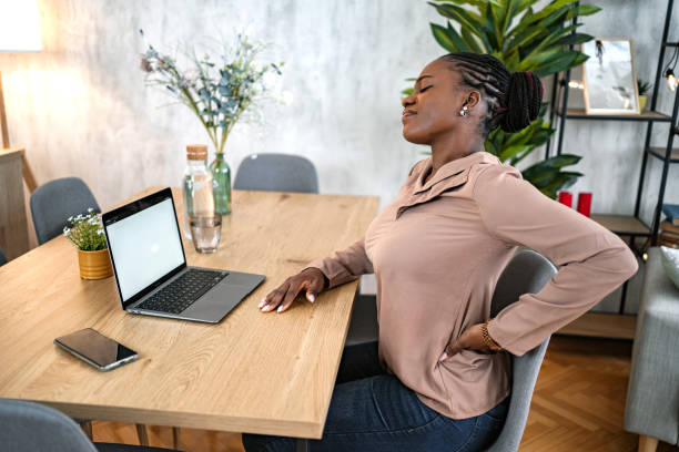 istock Black woman suffering from back pain while working on laptop at home 1573800376