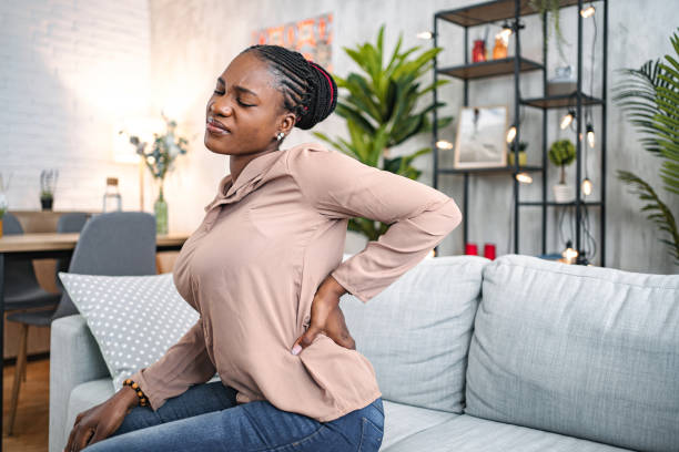black woman suffering with back pain while sitting at home - dor de costas imagens e fotografias de stock