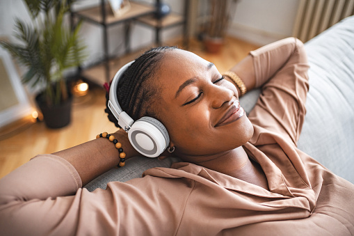 Black woman listening to music on her wireless headphones and relaxing on her living room sofa