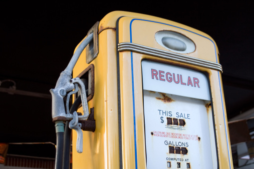 A gas station with 1940s fuel pumps and a vintage car. The photo is shot with a panoramic camera (Hasselbad XPAN), 45mm lens. The image is slightly toned to bring out the reds and yellows of the pumps.