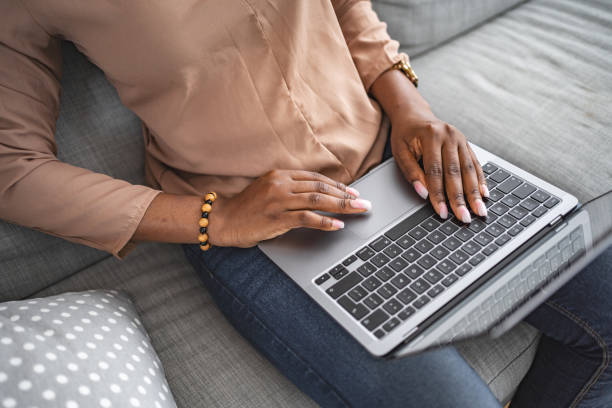 istock Black woman typing on her laptop keyboard while sitting on the sofa 1573803701