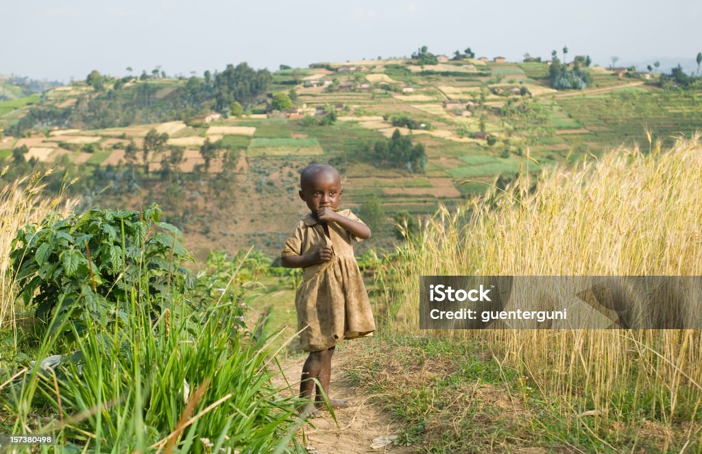 Young African tending to the fields among tall grass A young african girl standing on a path between wheat fields. Child Stock Photo