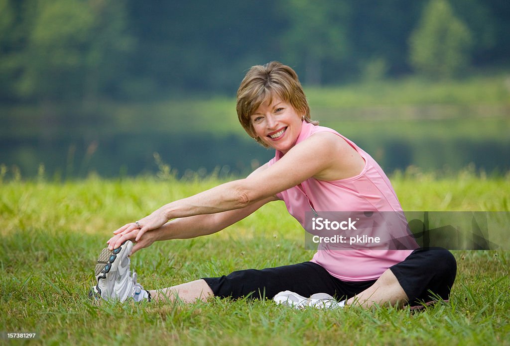 Mujer sonriente de estar y s'extiende más de piernas en el parque - Foto de stock de 60-64 años libre de derechos