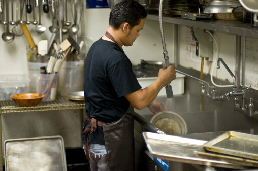 Hispanic male worker washing the dishes at a restaurant kitchen