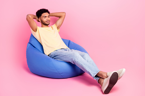 Full body length photo of dreaming sleeping young guy take nap hands head lying beanbag comfortable place isolated on pink color background.