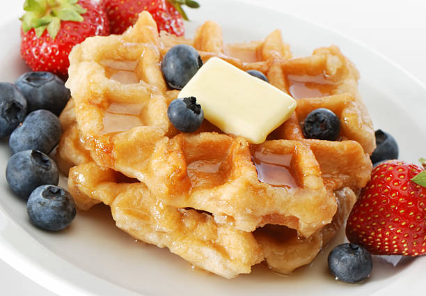 Stacks of waffles surrounded with berries, syrup and butter stock photo