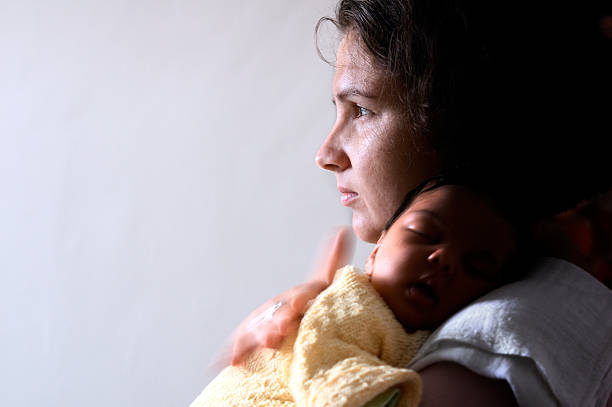 Worried Mother With Baby Newborn On Her Shoulders Royalty free stock photo of young mother carries her newborn baby on her shoulder. she looks worried. Use of window light. serious baby face stock pictures, royalty-free photos & images