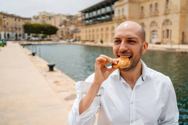 Handsome young man eating a savory Maltese pastry (pastizz) in Cospicua in Malta.