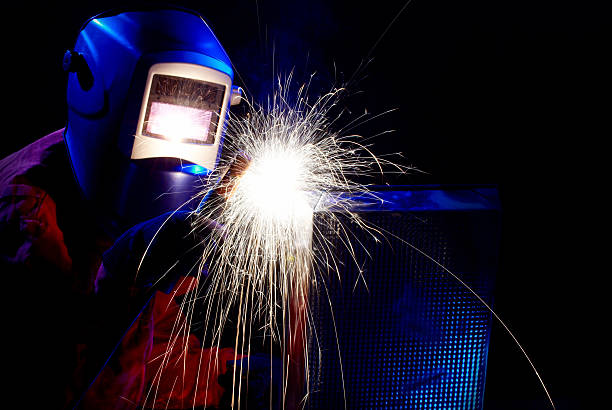 One male welder high up on a ladder, working on a steel welding project, with sparks flying everywhere.  low view, selective focus.
