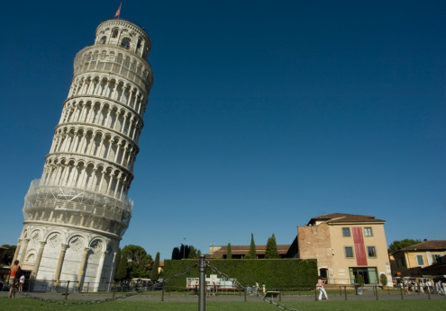 The leaning tower of Pisa showing how it leans in comparison to a straight regular built house. The Tower of Pisa (Torre di Pisa) is the campanile, or freestanding bell tower, of the cathedral of the Italian city of Pisa, known worldwide for its unintended tilt to one side. It is situated behind the Cathedral and is the third oldest structure in Pisa's Cathedral Square (Piazza del Duomo). Italy