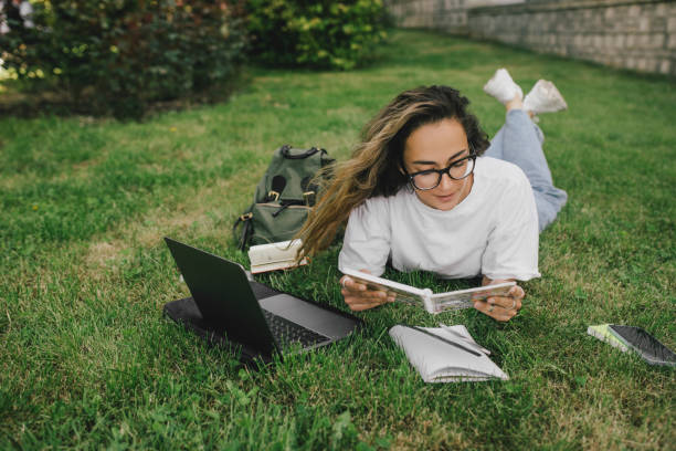 istock Young woman student studying using her books, laptop and notebook, sitting on grass. 1573866946