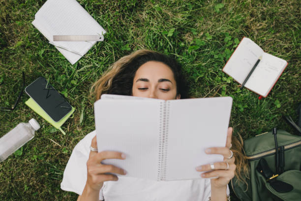 istock Young woman student studying using her books, laptop and notebook, sitting on grass. 1573866950