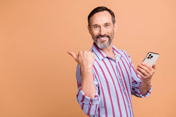 istock Photo of elderly man indicating empty space facebook twitter telegram instagram hold smartphone isolated on beige color background 1573869041