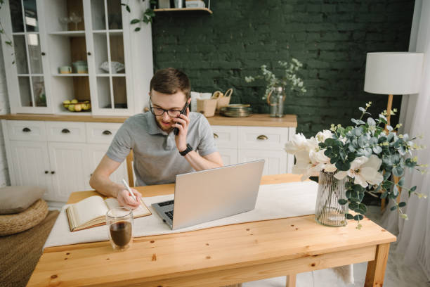 istock Writing in notebook. Serious man working, learning online on laptop in home office. Trading cryptocurrency. Trader talk on phone, investor broker analyzing indexes. Freelance. Marketing. Communication 1573875584
