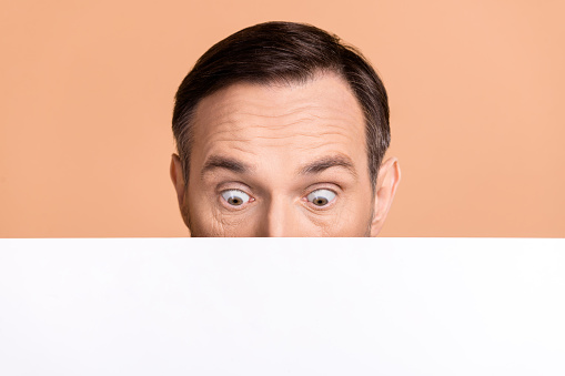 Portrait of speechless impressed person hide half face look interested down empty space blank isolated on beige color background.