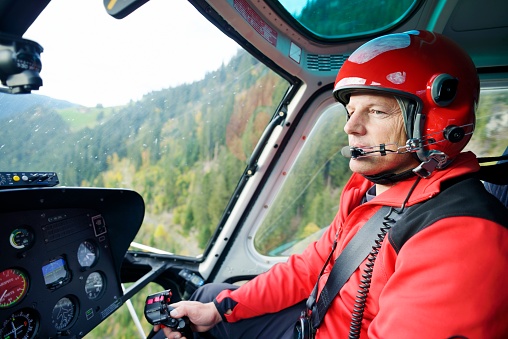 A male helicopter pilot concentrates on flying his aircraft in the Swiss mountains. The in-flight image showing the pilot, controls and instruments, was captured in the Swiss Alps, Bernese Oberland region. The helicopter is used for mountain rescue and general transportation.