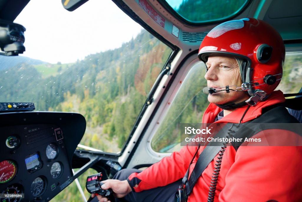 Male Pilot Flying Helicopter A male helicopter pilot concentrates on flying his aircraft in the Swiss mountains. The in-flight image showing the pilot, controls and instruments, was captured in the Swiss Alps, Bernese Oberland region. The helicopter is used for mountain rescue and general transportation. Helicopter Pilot Stock Photo