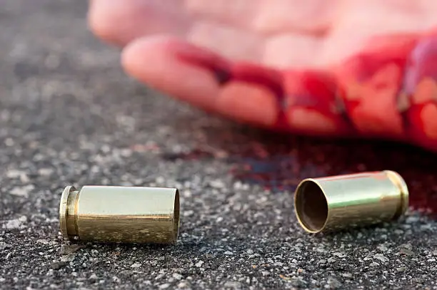 A man shot in the streets with the bullet casing laying next to a bloody hand.