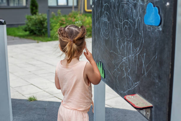 istock Little kid draws with white chalk on blackboard outside. Sensory experience. Baby development 1573915269