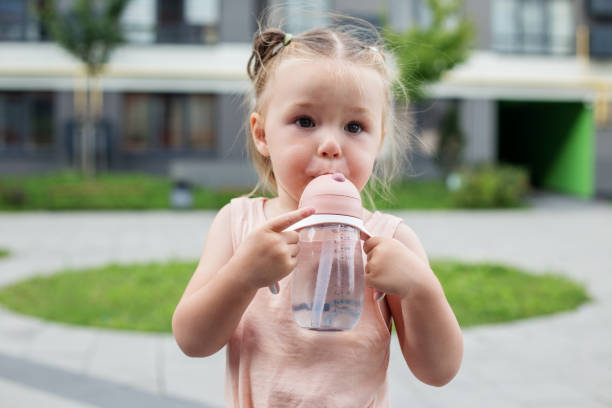 istock Toddler girl drinking water. Two year old. Sippy cup. 1573915293