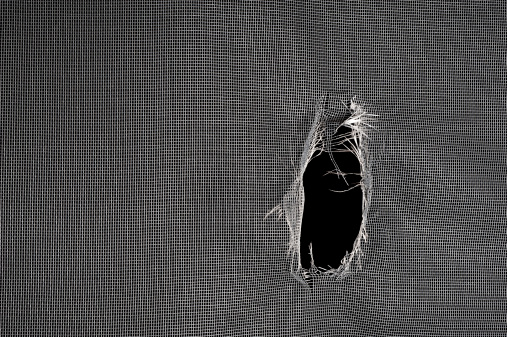 Window screen torn with a big hole against a black background.