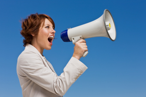 Businesswoman shouting in megaphone against sky