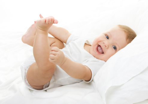 Happy smiling baby playing with his feet, on white background. 