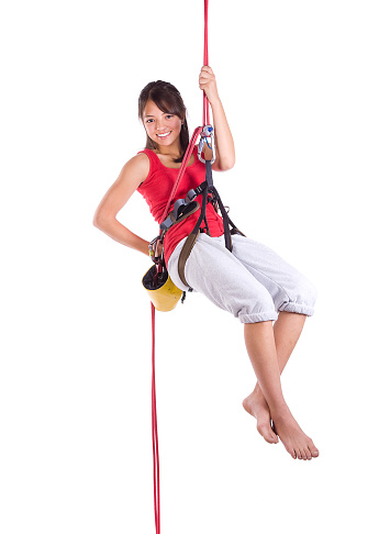A teenage girl in climbing gear rapelling against a white background.