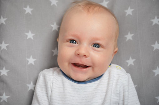 Portrait of smiling newborn baby with open mouth, close-up. Happy smiling child with blue eyes, looking at camera. Face expression.