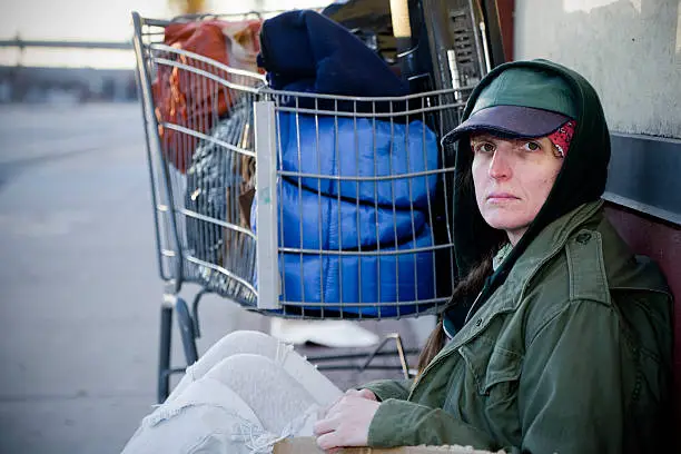 A homeless woman sitting on a sidewalk.