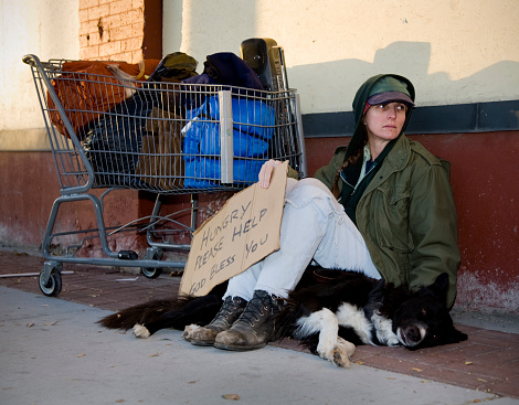 A homeless woman sitting on a sidewalk with her dog.