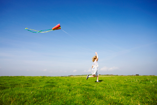 Little boy is playing outdoors at daytime. Standing, having fun with kite.