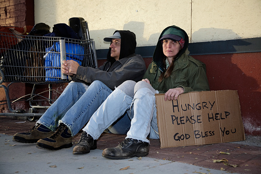 A homeless couple sitting on a sidewalk.