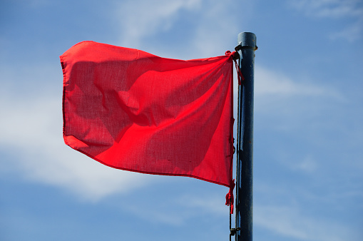 Red warning flag flutters in the breeze against a background of puffy clouds