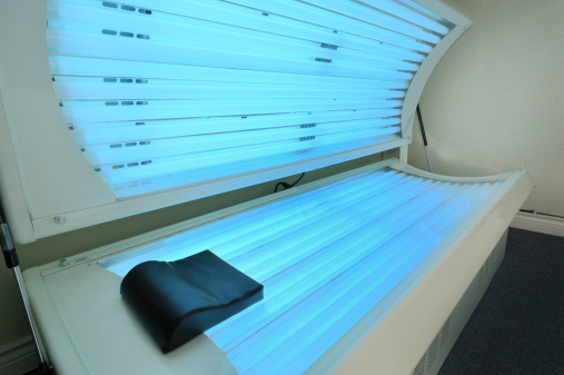 A tanning bed is open showing all it's lights.  Wide angle view.  Lights show a bright blue and there is a black head rest.