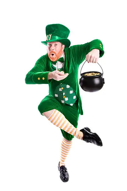 Full length photograph of a leprechaun holding gold in his hand and in his pot; he's dancing a jig; copy space