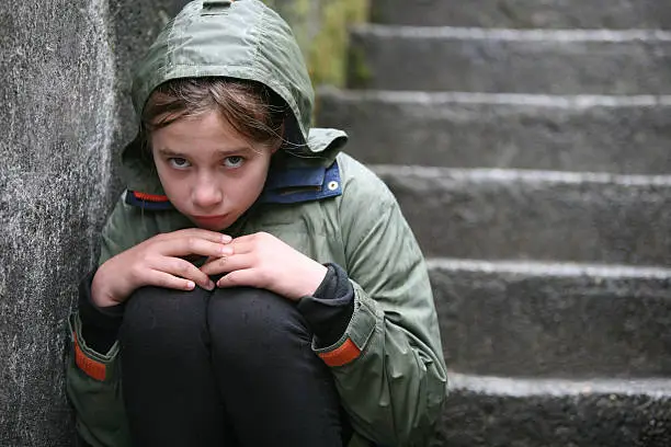 Forlorn Little Girl Sits in a Huddle on Some Old Stone Stairs