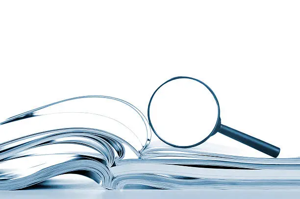 Photo of Searching, opened magazines and magnifier glass, side view, isolated white