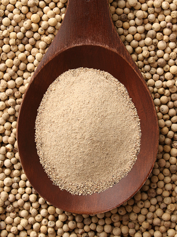 Top view of wooden spoon full of ground white pepper