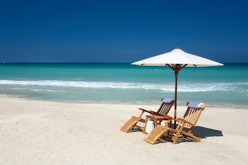 two teak chairs with white umbrella on a beach in Florida