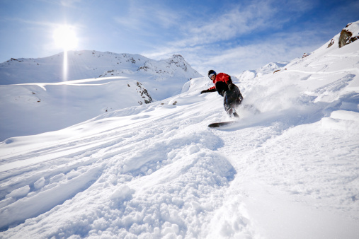 A snowboarder going downhill in the snow in the Alps